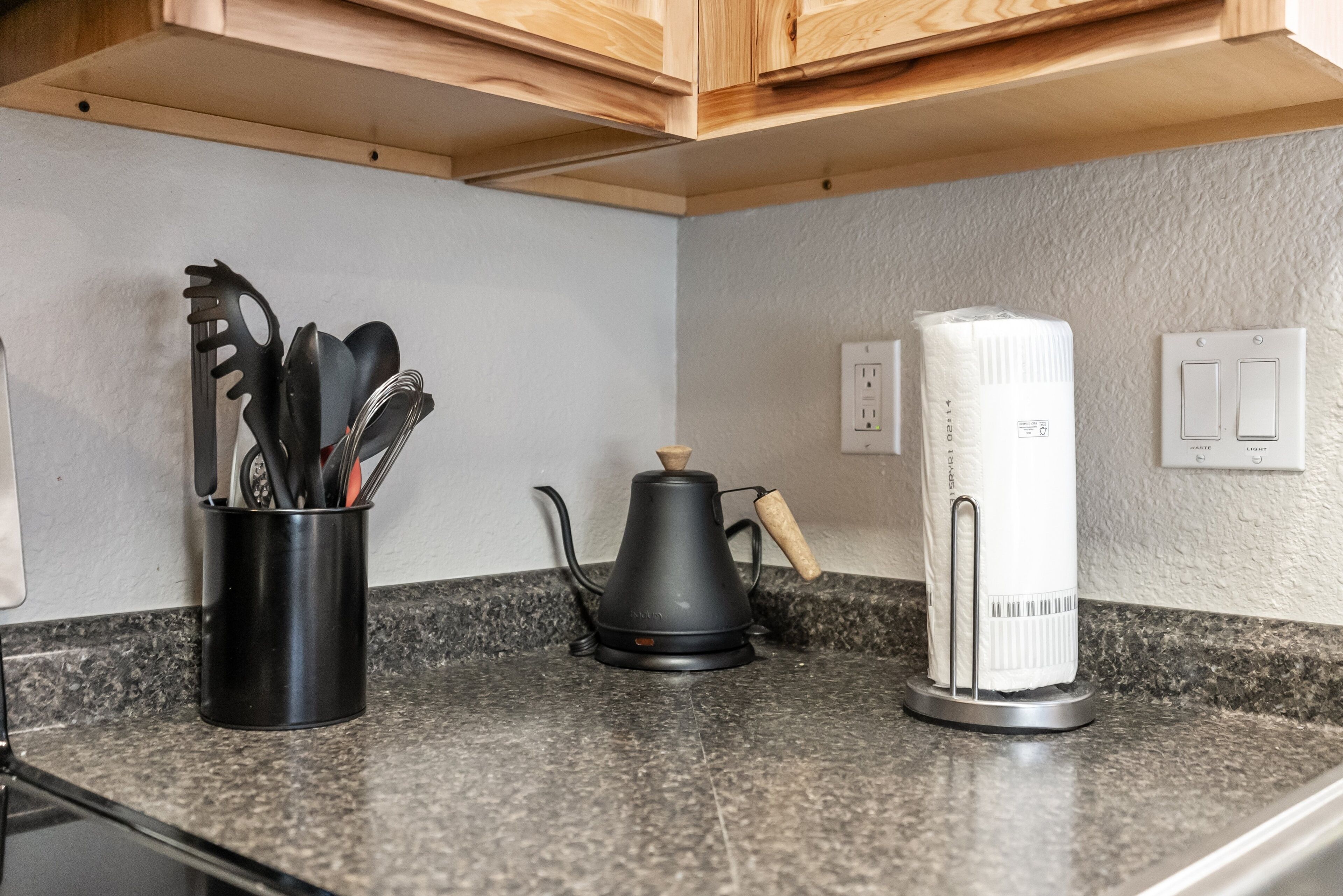 A kitchen counter with a coffee maker, a paper towel dispenser, and a utensil holder.