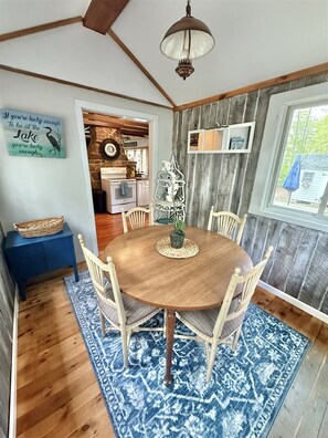 Un comedor con una mesa y sillas de madera, un tapete azul estampado y una pared rústica con techo de madera.