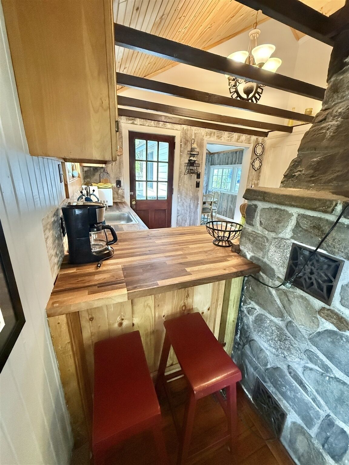 Une cuisine rustique avec une cheminée en pierre, un comptoir en bois et des tabourets de bar rouges.