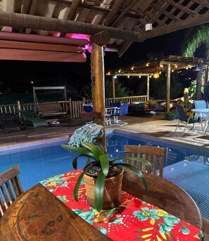An outdoor pool area with a wooden table, chairs, and a potted plant.