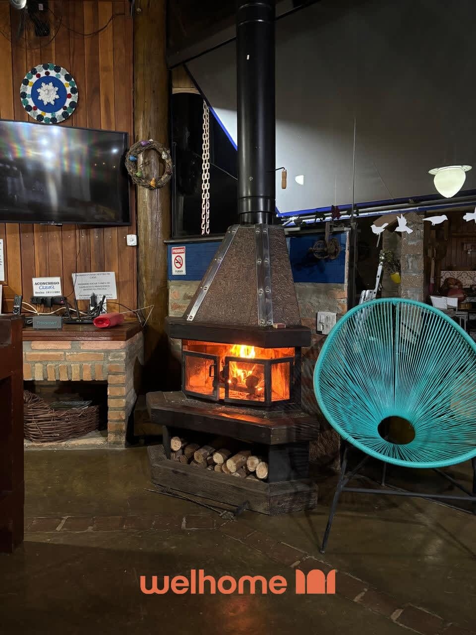 Un poêle à bois avec une cheminée, un téléviseur fixé au mur et un ventilateur bleu.