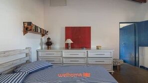 Une chambre à coucher avec un lit, une commode, un mur d’accent rouge et une porte bleue.