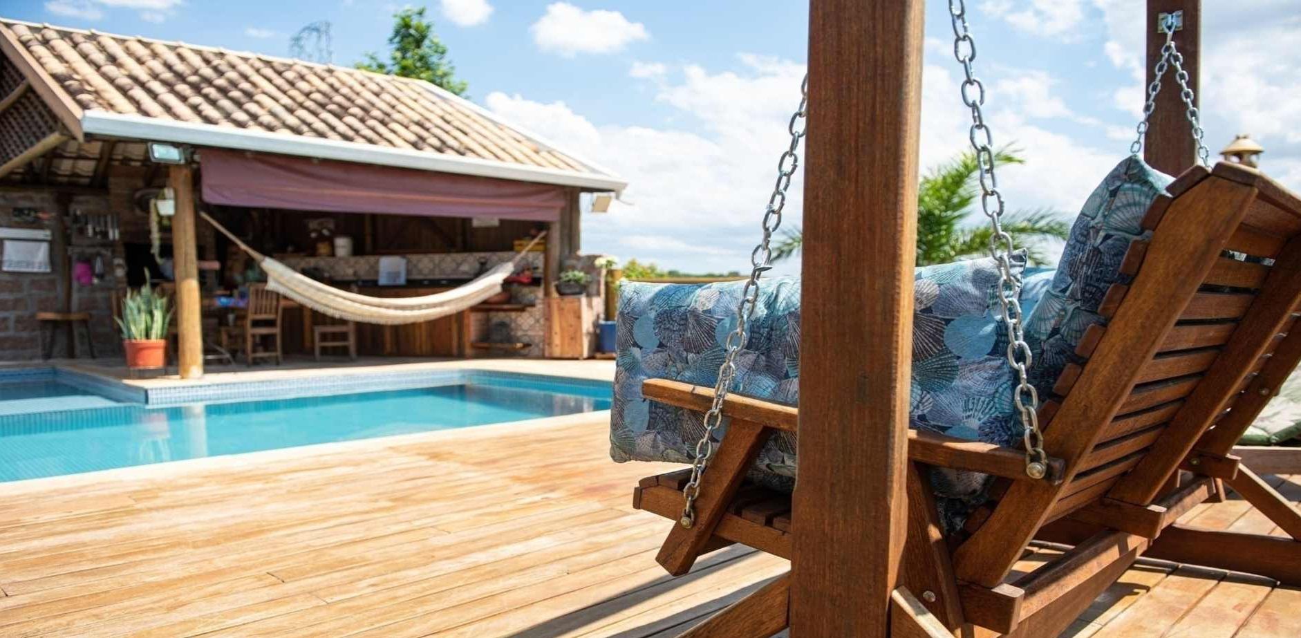 A wooden deck with a pool, a swing chair, and a building with a tiled roof.
