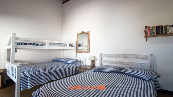 A room with two bunk beds, a bedside table with a lamp, a mirror, and a bookshelf with books.