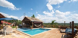 Eine Holzterrasse mit Schwimmbecken, ein kleines Steinhaus mit Ziegeldach und einer Hängematte.