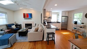 A modern living room with a fireplace, a sofa, a coffee table, and a dining area with a wooden table and chairs. - Steps to McKinley Beach walk to all in Union Pier Fire Pit (Union Pier)