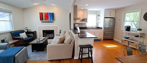 A modern living room with a fireplace, a sofa, a coffee table, and a dining area with a wooden table and chairs.