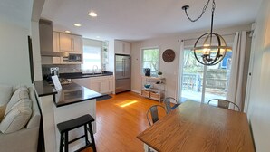 A modern kitchen with white cabinets, stainless steel appliances, and a wooden dining table. - Steps to McKinley Beach walk to all in Union Pier Fire Pit (Union Pier)