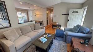 A living room with a beige sofa, a blue sofa, a coffee table, and a door with a coat rack. - Steps to McKinley Beach walk to all in Union Pier Fire Pit (Union Pier)