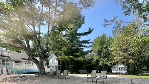 A sandy beach area with several beach chairs and a large tree providing shade.