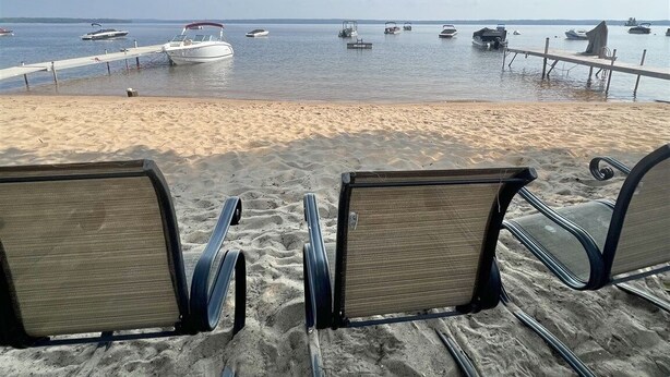 A beach with rows of empty beach chairs facing the sea, a sandy shore, and several boats anchored in the water.