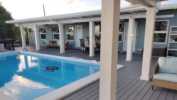 A swimming pool with a robotic toy on the edge, surrounded by a deck with outdoor furniture and a covered area with chairs and tables. - Charming 1-Bedroom Apartment on Beautiful St. Croix, USVI with Pool & Ocean View (Christiansted)