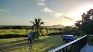 A deck with a view of a grassy area, a palm tree, and a car parked nearby. - Charming 1-Bedroom Apartment on Beautiful St. Croix, USVI with Pool & Ocean View (Christiansted)