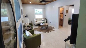 A spacious living area with a high ceiling, a sofa, a green armchair, a coffee table, and a television. - Charming 1-Bedroom Apartment on Beautiful St. Croix, USVI with Pool & Ocean View (Christiansted)