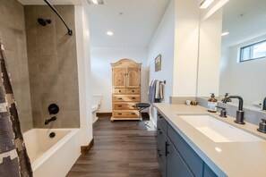 Un baño moderno con bañera, un mueble de madera y un espejo grande.