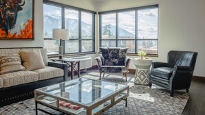 A modern living room with a sofa, armchair, and coffee table. Large windows offer a mountain view. - Downtown Penthouse Condo – For 6! (Columbia Falls)