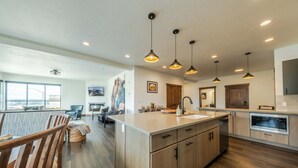 A modern kitchen with a central island, pendant lighting, and a large window providing natural light. - Downtown Penthouse Condo – For 6! (Columbia Falls)