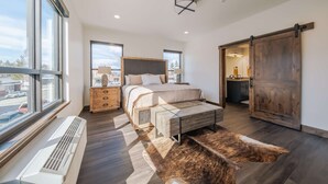 Ein modernes Schlafzimmer mit einem großen Bett, einer hölzernen Kommode, einem Glastisch und einer Schiebetür im Bauernhausstil.