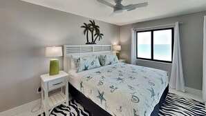 Une chambre à coucher comprenant un lit, des tables de chevet, un ventilateur de plafond, une fenêtre avec des rideaux et un tapis à motifs zébrés.