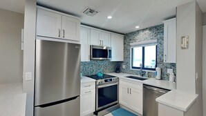 Une cuisine moderne dotée d’appareils électroménagers en acier inoxydable, de meubles blancs et d’un revêtement mural bleu.