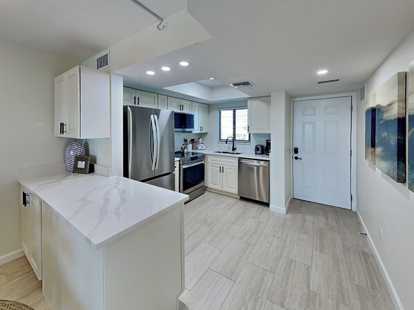 A modern kitchen with white cabinets, stainless steel appliances, and a light wood floor.