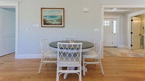A dining area with a round table and four white chairs, a framed painting on the wall, and a door leading to another room. - Life of Reilly - Private & Serene Rockport Escape (Rockport)