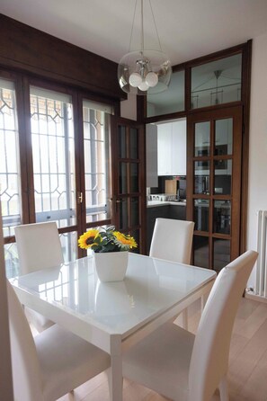 A dining area with a white table and chairs, a vase with sunflowers, and a kitchen in the background. - HouSmart Isonzo 6 (Casalecchio di Reno)