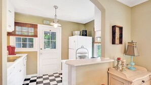 Une cuisine avec un carrelage à motifs, des meubles blancs, un réfrigérateur et une petite table à manger.
