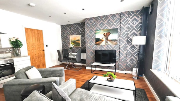 Ein modernes Wohnzimmer mit grauen Sofas, einem Essbereich, einem Fernseher und einem Kamin.