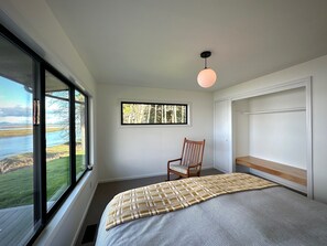 Enjoy a serene view of the water and lush surroundings from this cozy bedroom with a single bed, comfortable seating area, and natural light.