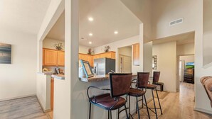 A modern kitchen with wooden cabinets, a stainless steel refrigerator, and a bar area with bar stools. - The Nest on Birdie Lane - For 8! (Branson West)