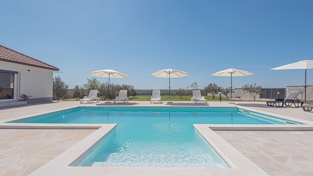A rectangular swimming pool with clear blue water, surrounded by lounge chairs and umbrellas.