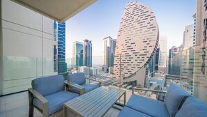 A modern balcony with a city view, featuring a sofa, a table, and a glass railing. - Premium 1BR Apt Missoni Urban Oasis (Dubai)