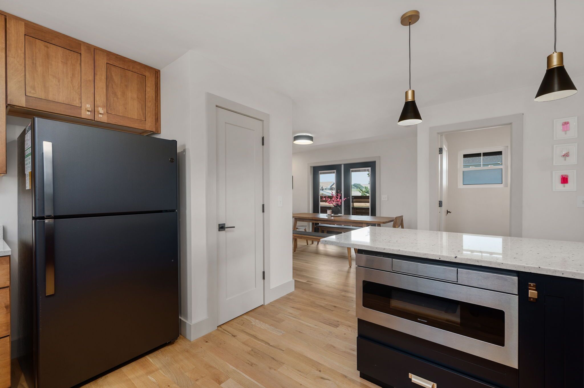 Una cocina moderna con un refrigerador negro, armarios de madera, un comedor con mesa y sillas, e iluminación colgante.