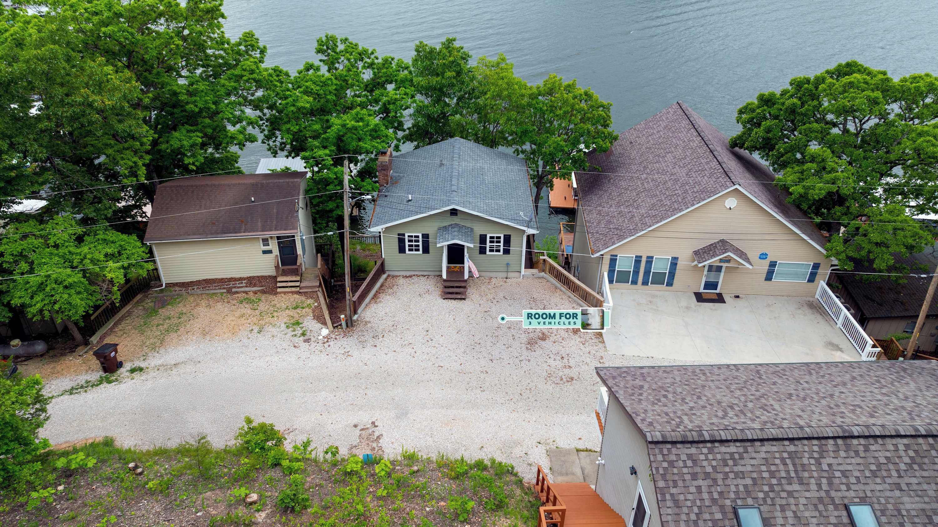 A residential area with houses, a sign indicating a room for 3 vehicles, and a body of water in the background.