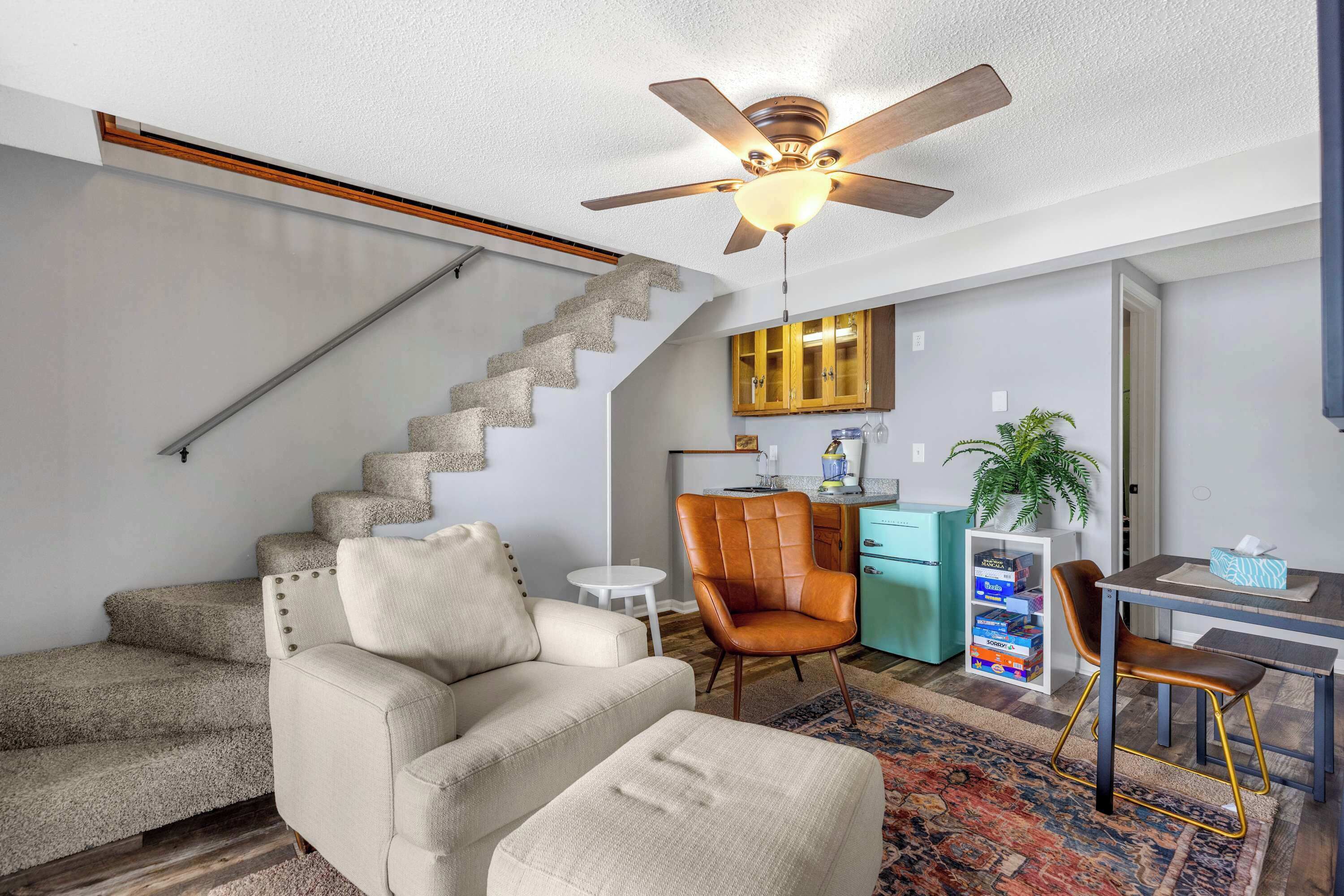 Una sala de estar con sofá, otoman y comedor con mesa y sillas. Se ve una escalera que conduce a otro nivel.