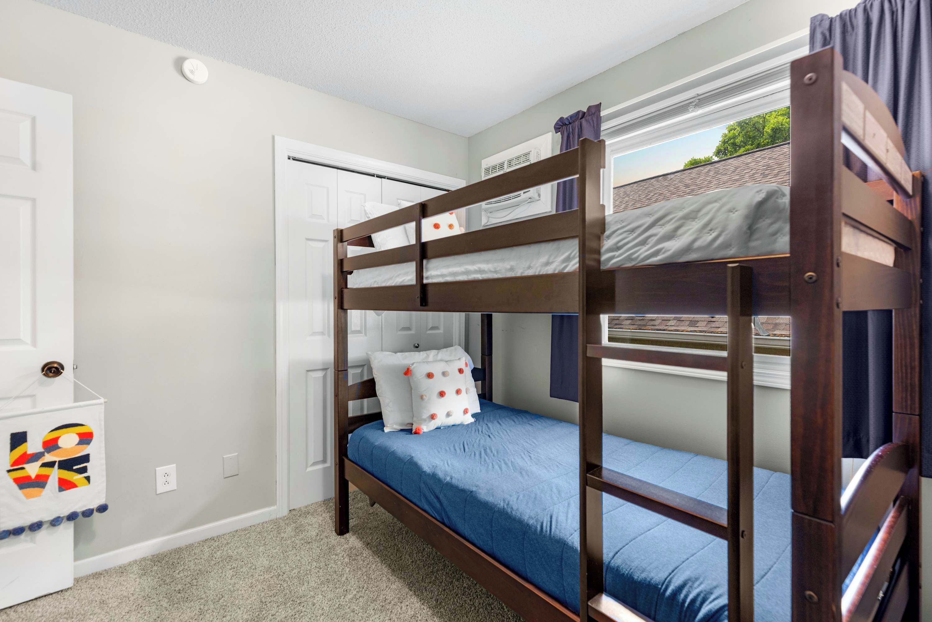 Un lit superposé avec un matelas bleu, une porte blanche et une petite armoire blanche sur laquelle est posée une serviette colorée.