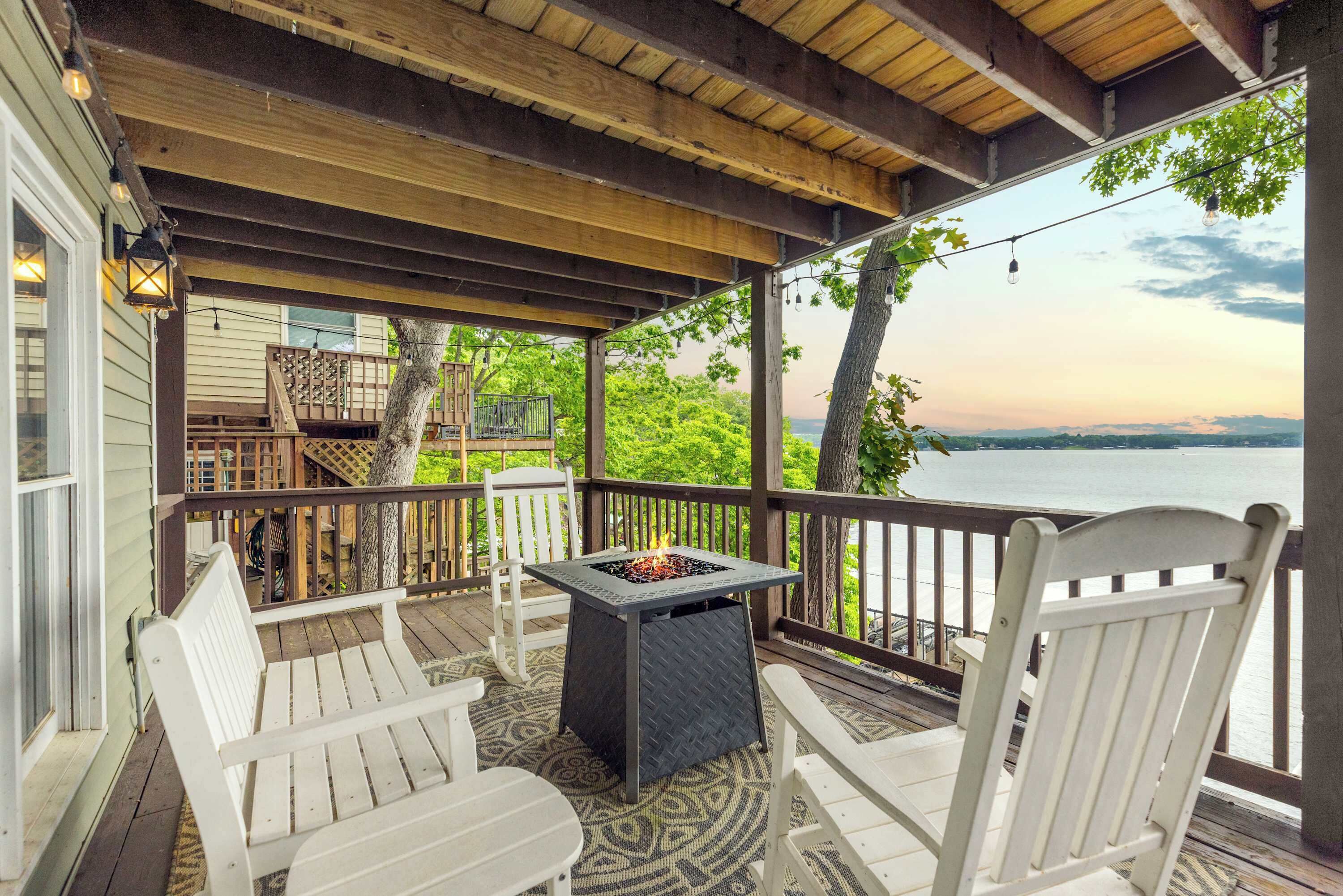 A covered deck with white chairs, a fire pit, and a view of the water.