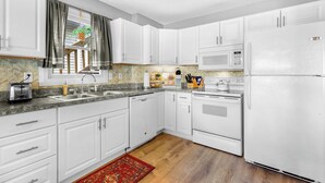 A modern kitchen with white cabinets, a granite countertop, a microwave, a stove, and a dishwasher. - Dockside Dream w/ Kayak & Dock (Rocky Mount)