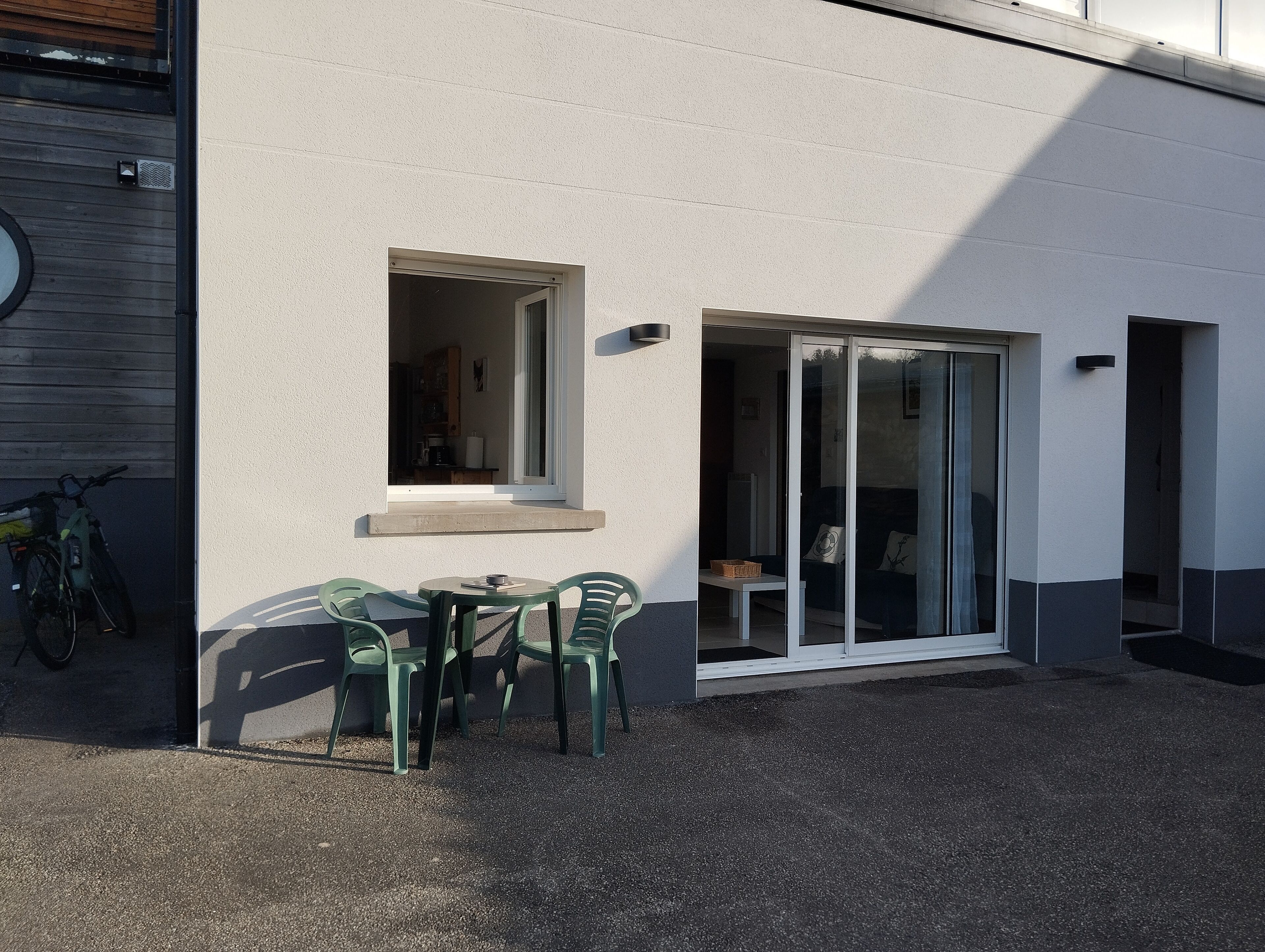 A building with a small window and a sliding glass door leading to an outdoor seating area with a table and chairs.