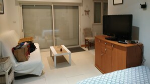 Een woonkamer met een bank, een bijzettafeltje, een televisie op een houten kast, een rieten mand en een rieten stoel.