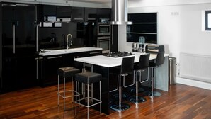A modern kitchen with black cabinets, a white countertop, and a stainless steel range hood. There are four bar stools and a small kitchen island with a gas stove.