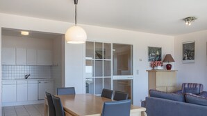 A modern kitchen with white cabinets, a dining table with chairs, and a sofa in a living area.