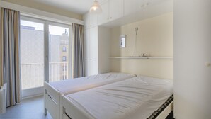 A bedroom with a bed, a window with curtains, a ceiling light, and a small shelf with a picture.
