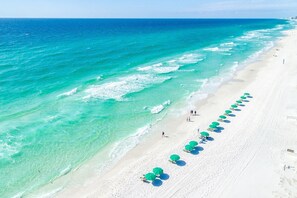 A beach with clear turquoise waters and a row of green umbrellas along the shore. - Private Pool-Steps to Sugar Sand and Sunset Views (Destin)