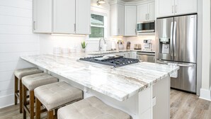 A modern kitchen with white cabinetry, a marble island, a stainless steel refrigerator, and a built-in oven. - Private Pool-Steps to Sugar Sand and Sunset Views (Destin)