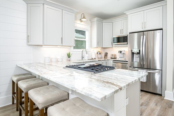 A modern kitchen with white cabinetry, a marble island, a stainless steel refrigerator, and a built-in oven. - Private Pool-Steps to Sugar Sand and Sunset Views (Destin)