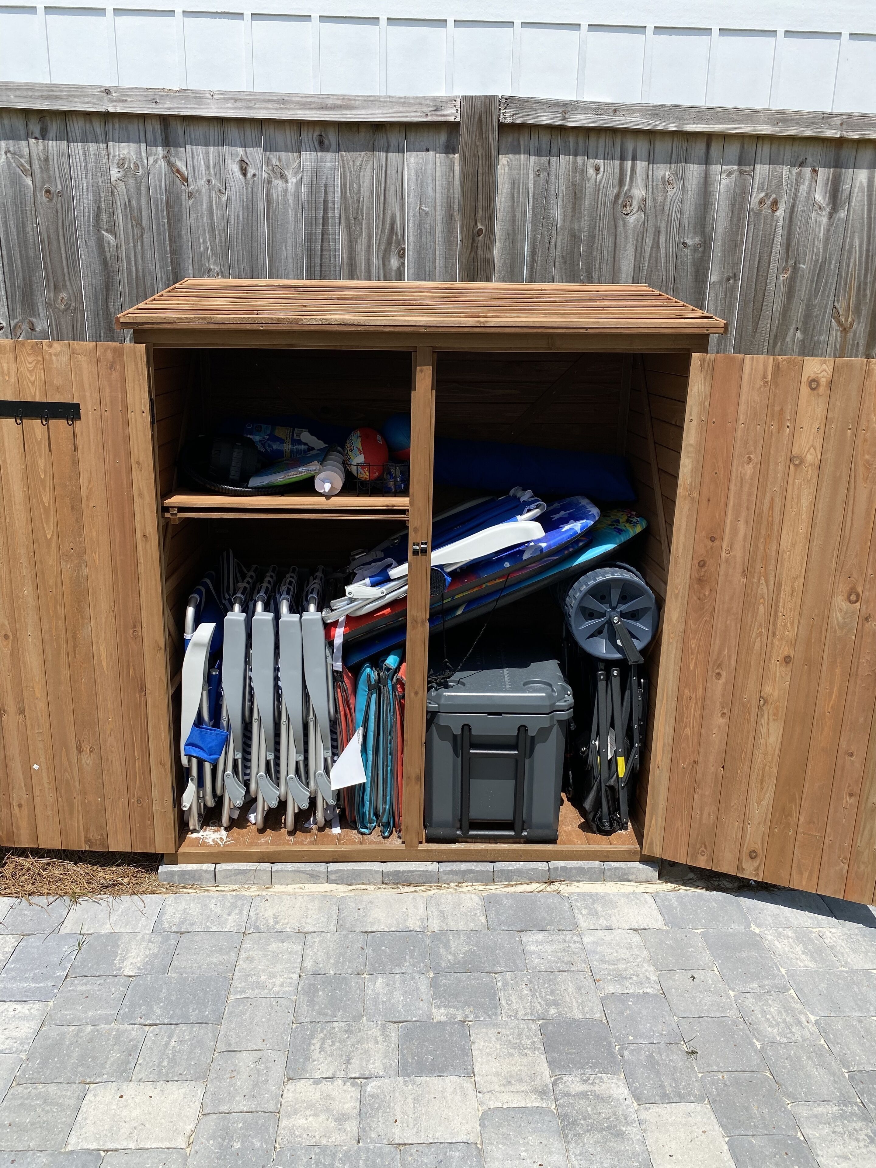 Een houten tuinhuis met een schuin dak, met daarin diverse spullen zoals peddels, een kajak en een opbergkist.