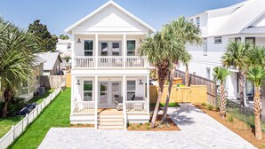 A two-story white house with a balcony, a covered front porch, and a paved driveway. - Private Pool-Steps to Sugar Sand and Sunset Views (Destin)