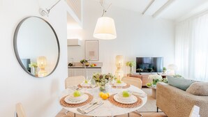 Una sala de estar moderna con una mesa de comedor redonda preparada para cuatro personas, un sofá y un televisor.